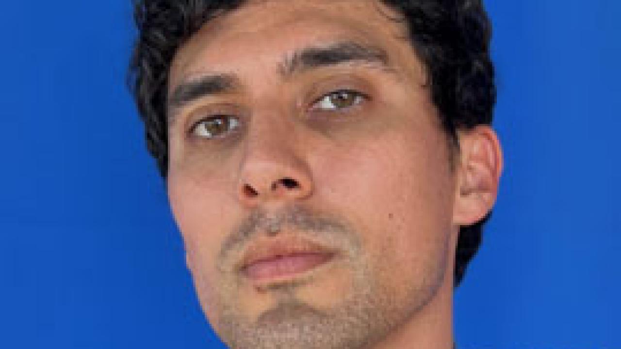 A man with short black curly hair looking at the camera