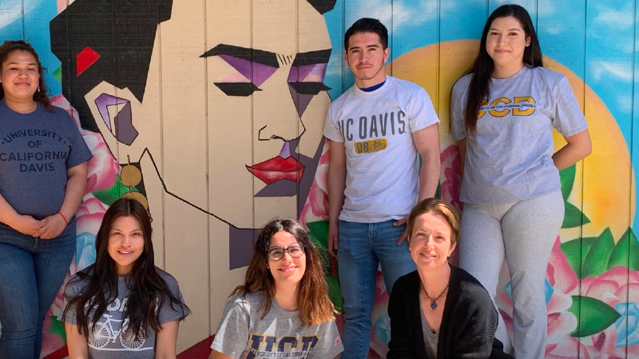 A group of people pose in front of a mural of Frida Kahlo 