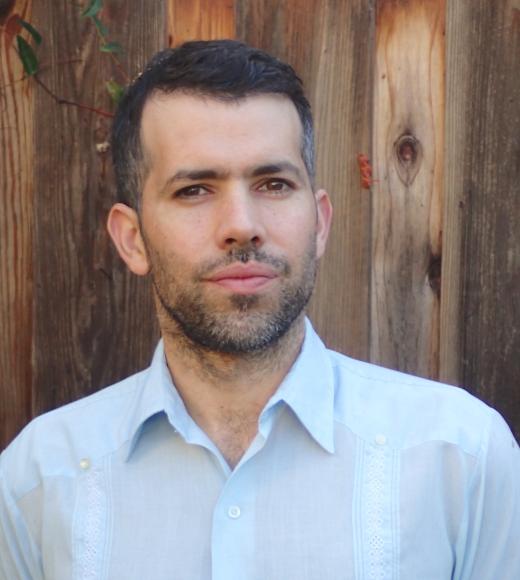 A photo of a man wearing a white shirt in front of a tall wooden fence.