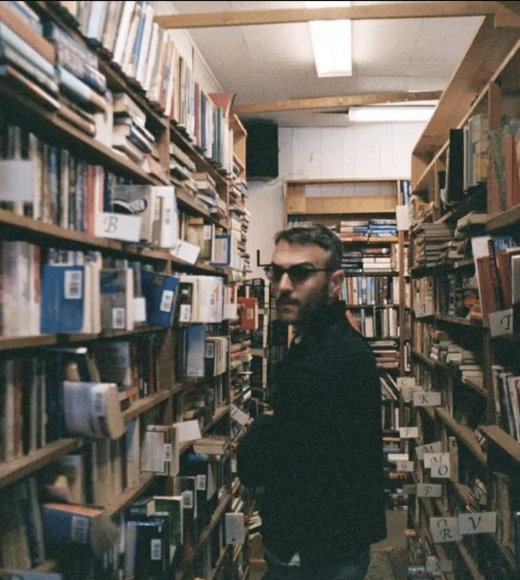 A man wearing glasses between two crowded bookshelves