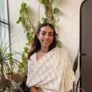 Smiling young woman seated by houseplants, wearing cream shawl and blue choker